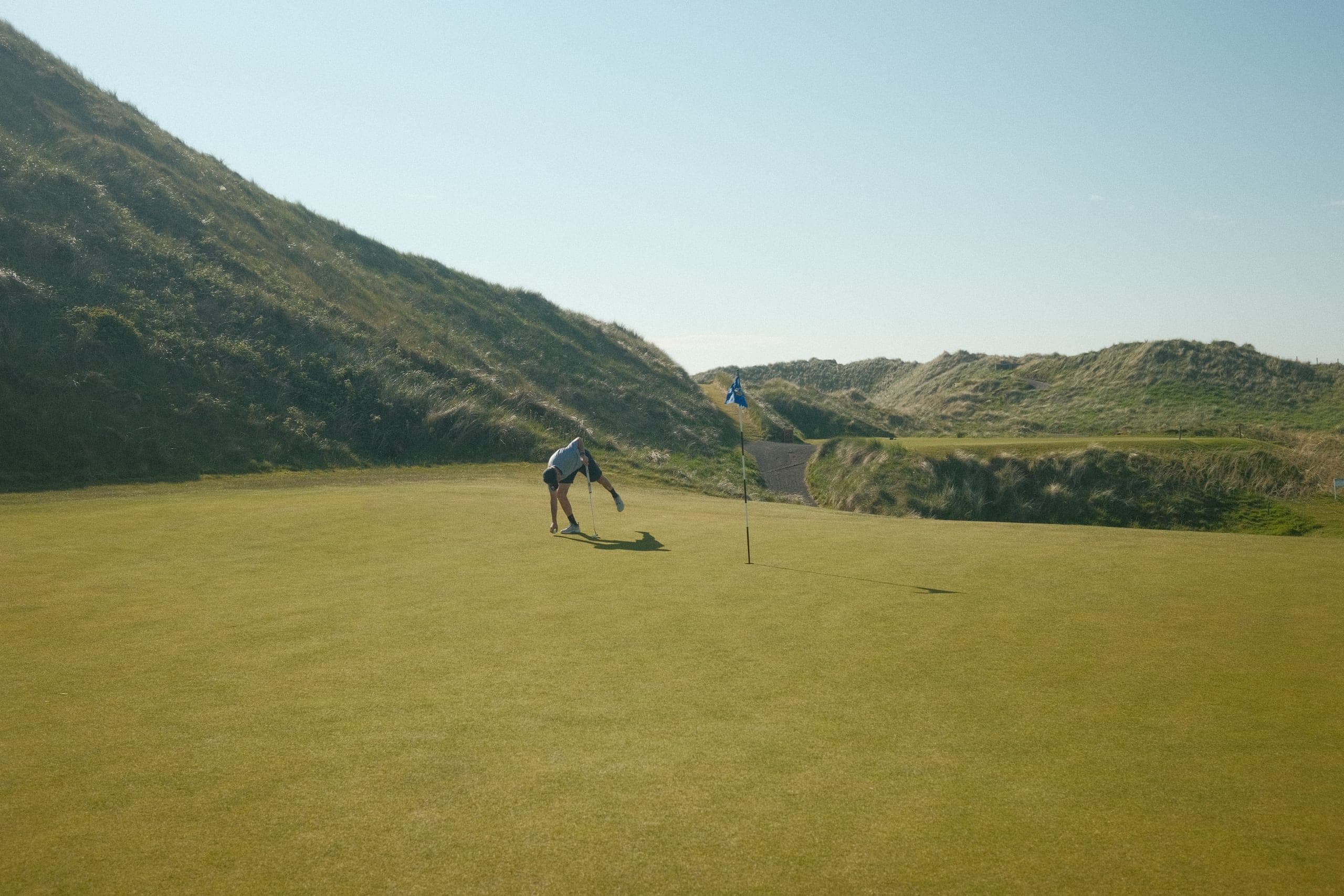 A player crouching to mark a ball on a links green.