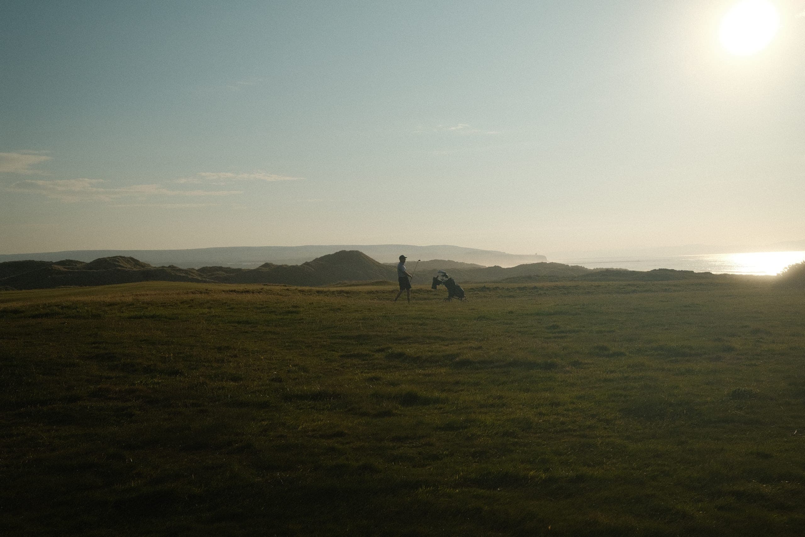 A golfer silhouetted against low sun on an empty seaside links.