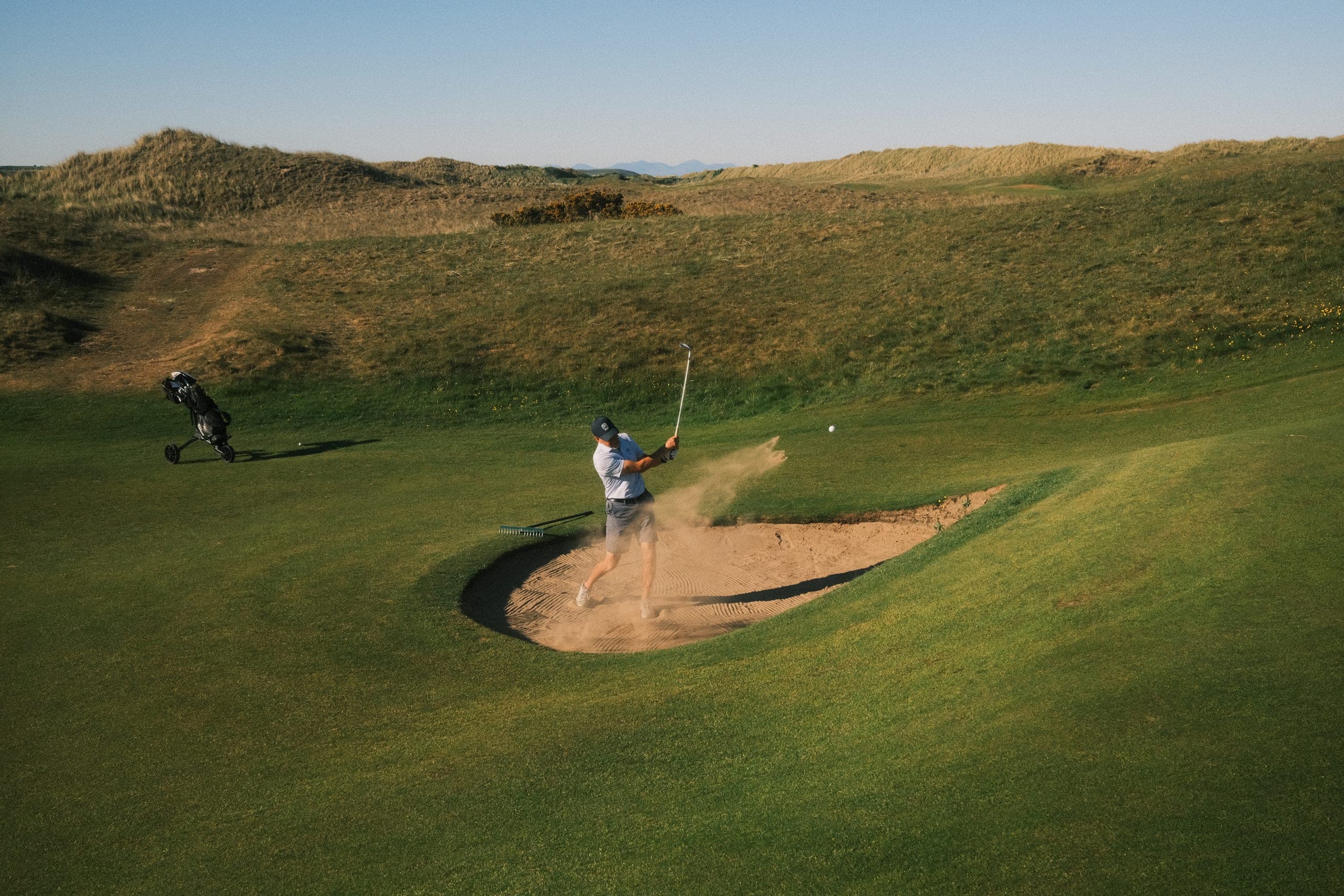 A player splashing out of a links bunker, sand mid-air.
