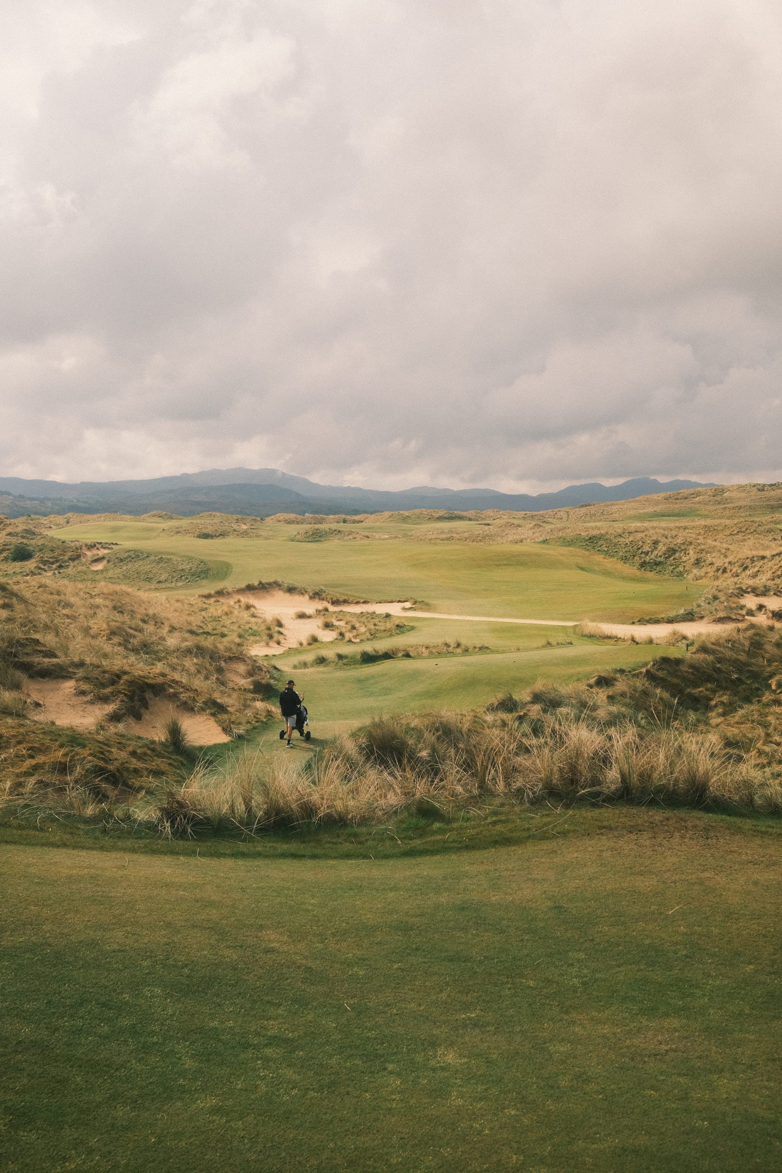 A golfer alone in a dunes valley under moody cloud.